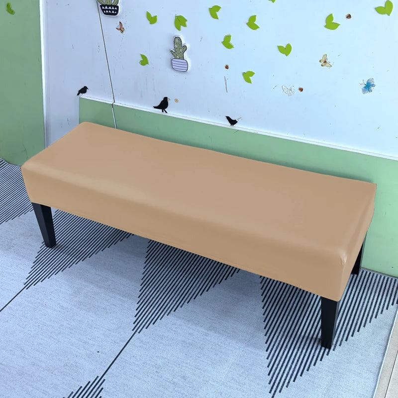 A beige stretch pu leather waterproof bench slipcover placed on a light-colored floor in a room with a white wall and green t