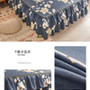 A navy blue printed bed skirt featuring white and yellow floral patterns on a bed.