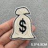 A beige embroidered iron-on patch shaped like a money bag with a dollar sign on it being held in a hand.