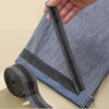 A hand is applying black self-adhesive hem tape to the bottom edge of a blue denim pant leg for repair.