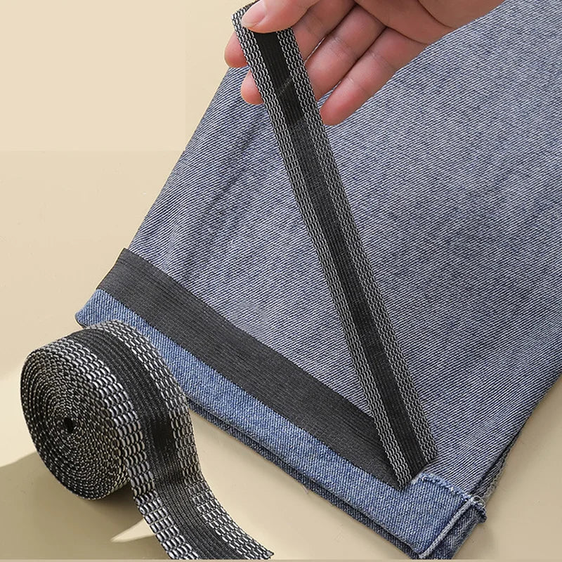 A hand is applying black self-adhesive hem tape to the bottom edge of a blue denim pant leg for repair.