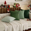 A set of four textured green throw pillow covers displayed on a light-colored sofa with rustic decor.