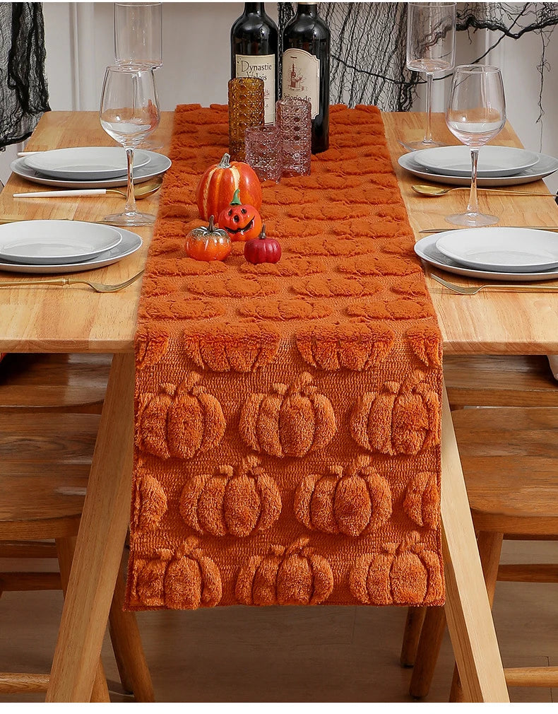 An orange textured table runner decorated with carved pumpkins and small gourds on a wooden dining table.