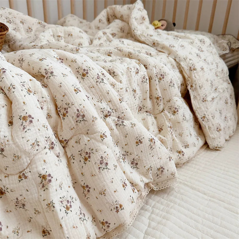 A soft, cream-colored muslin blanket with a delicate floral print is draped on a light surface.