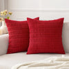 Two textured red corduroy throw pillow covers resting on a white sofa with a white blanket.