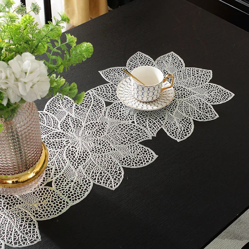 A white porcelain teacup and saucer rest on a decorative white lace placemat on a black table.