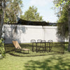 A large outdoor mosquito netting is stretched over a frame in a grassy yard, with a table and chairs set up underneath.