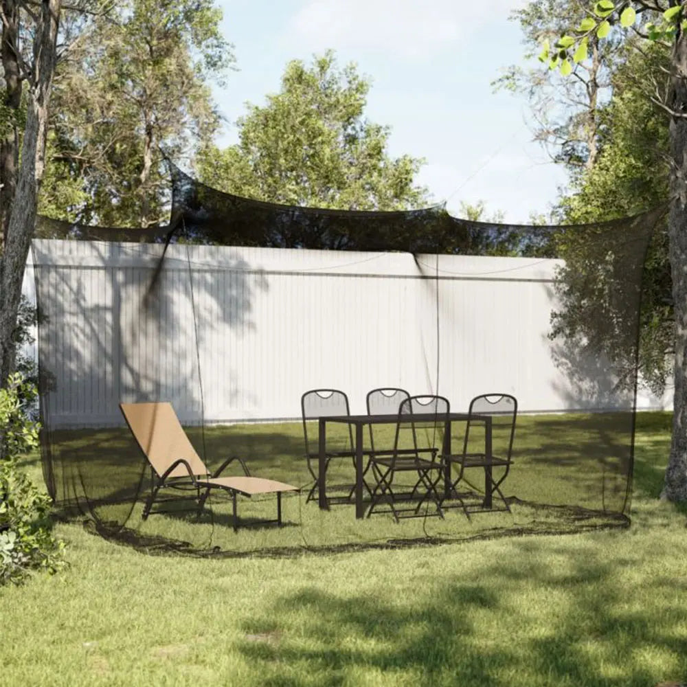 A large outdoor mosquito netting is stretched over a frame in a grassy yard, with a table and chairs set up underneath.