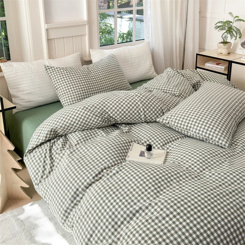 A set of three plaid duvet covers and pillowcases in sage green and white checkered patterns on a bed.