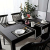A black dining table set featuring geometric placemats, cutlery, and a table runner with white porcelain dishes.
