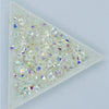 A pile of clear and iridescent crystal AB flatback rhinestones displayed in a white square tray.