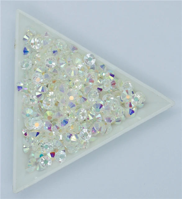 A pile of clear and iridescent crystal AB flatback rhinestones displayed in a white square tray.