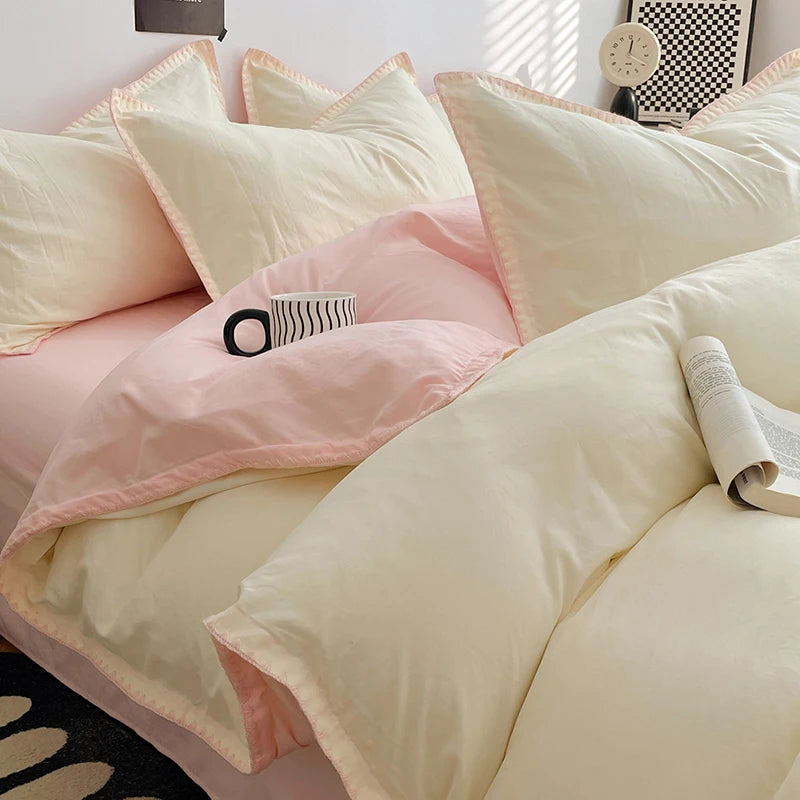 A close-up of a luxurious four-piece bed linen set featuring pale pink and cream colored pillows and duvet cover.