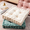 A stack of square cotton throw pillows in cream and sage green colors resting on a pink upholstered cushion.