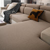A beige stretchy polar fleece sofa cover with a textured weave and an orange patterned throw pillow on a sectional sofa.
