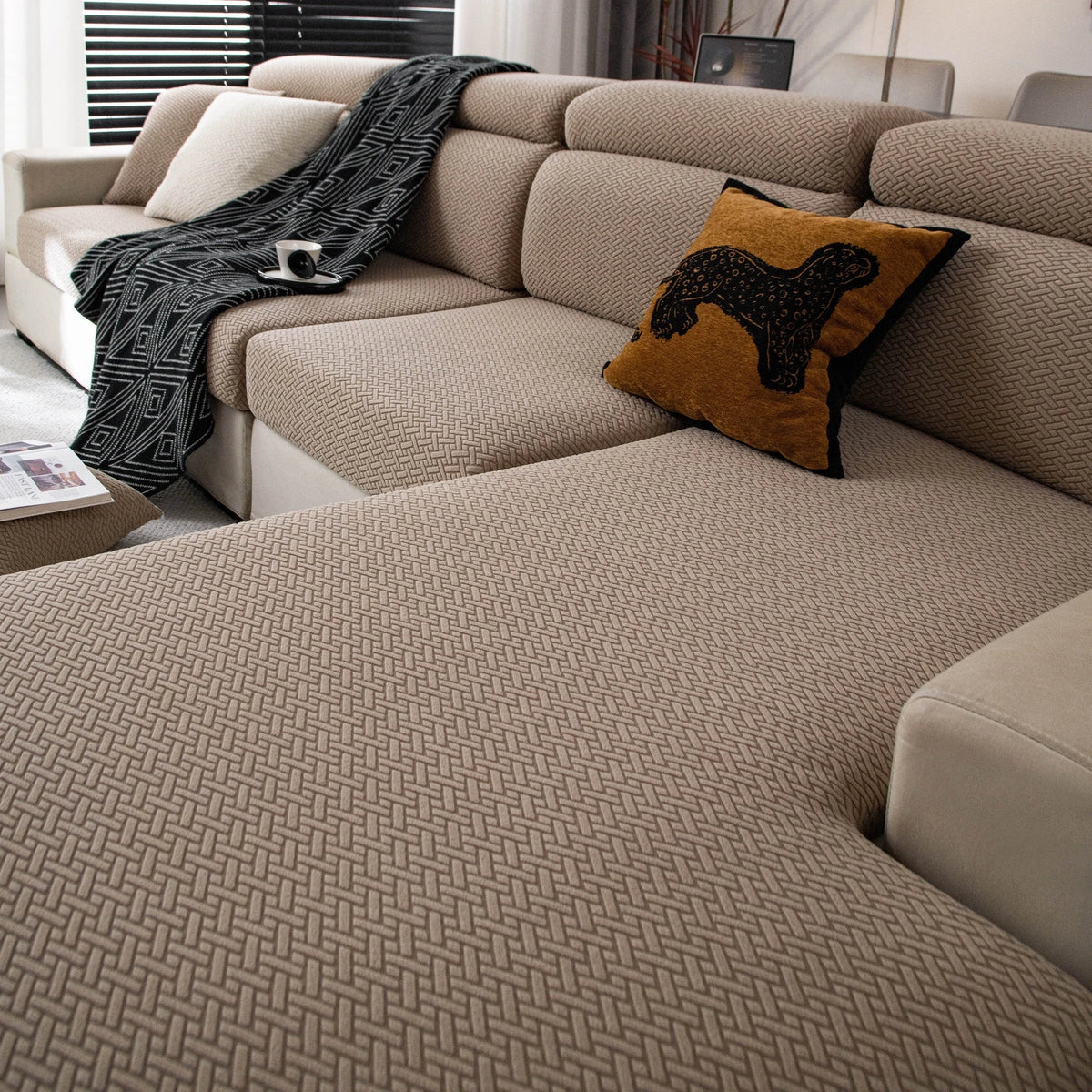 A beige stretchy polar fleece sofa cover with a textured weave and an orange patterned throw pillow on a sectional sofa.