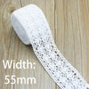 A roll of white cotton embroidered lace trim with a width of 55mm lying on a wooden surface.