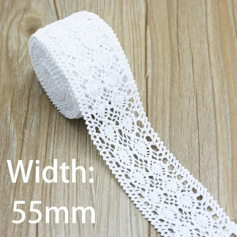 A roll of white cotton embroidered lace trim with a width of 55mm lying on a wooden surface.