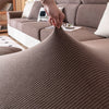 A close-up of a brown removable jacquard seat cushion cover being touched on a sofa.