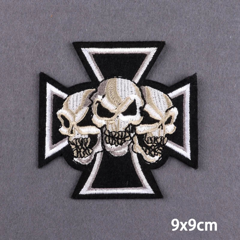 Black and white embroidered cross patch featuring three skulls on a gray background