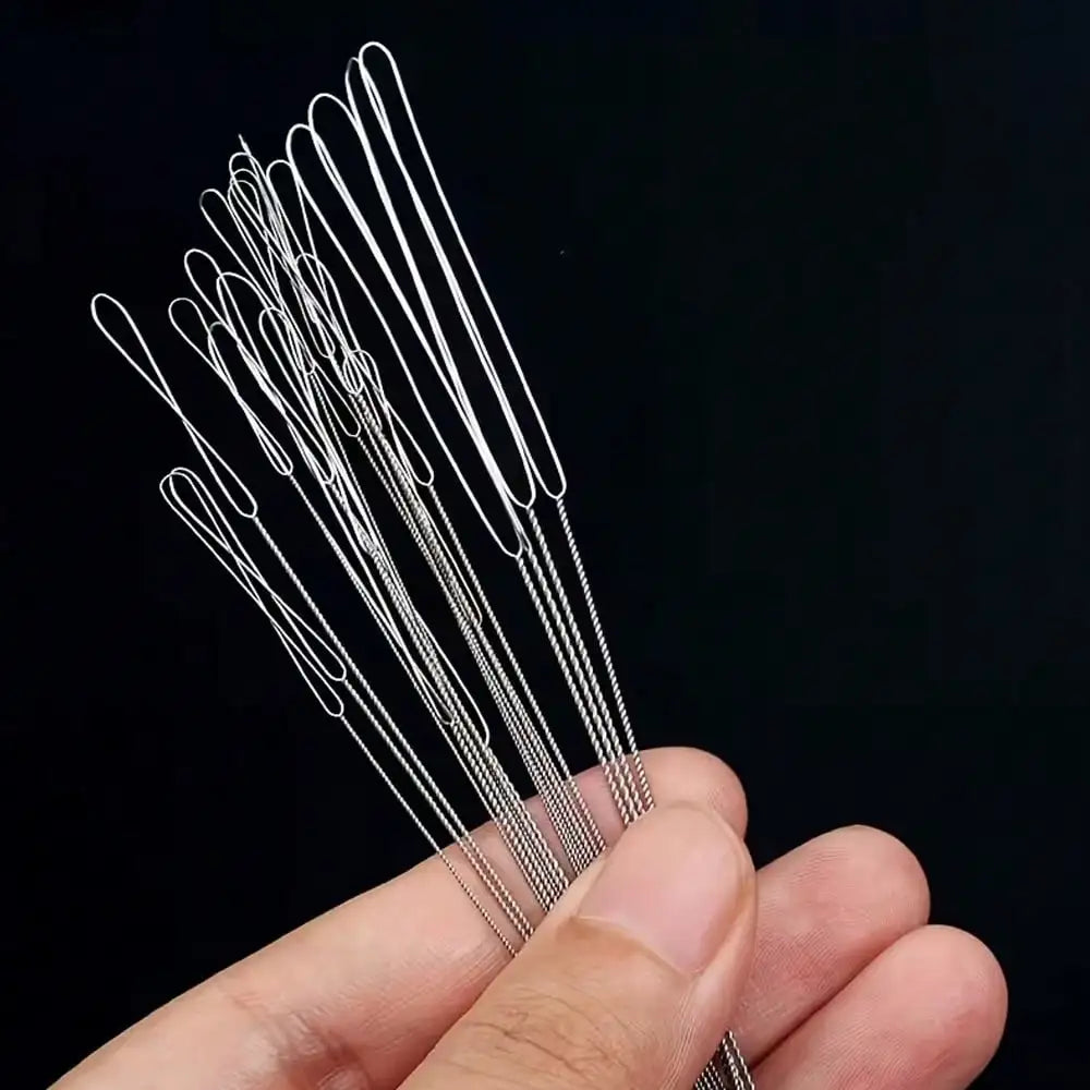 A hand holds a set of precision beading needles for jewelry making, showing the fine metal tools.
