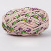 A ball of hand-dyed fabric strip yarn featuring a pink background with purple and green floral patterns.