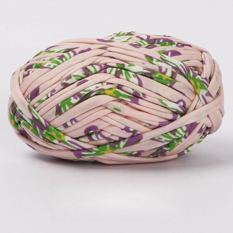 A ball of hand-dyed fabric strip yarn featuring a pink background with purple and green floral patterns.