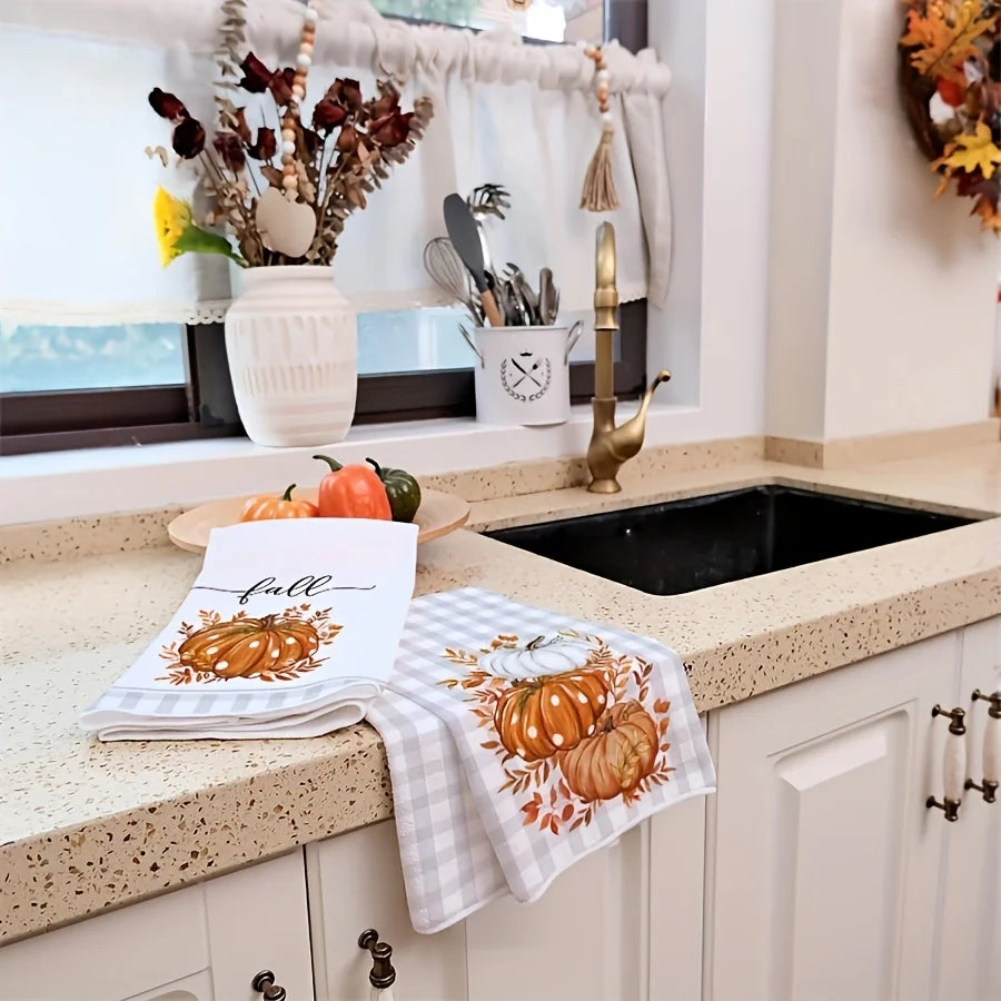 A pumpkin print kitchen towel draped over a sink counter next to various kitchen tools and seasonal decor.