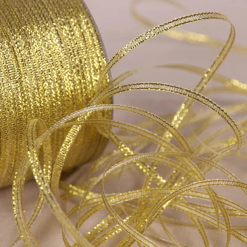 A close-up of gold and silver glitter satin ribbon spilling out, with a large spool visible in the background.