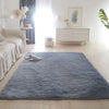 A fluffy blue gray area rug placed on a light wood floor in a bright, modern room.