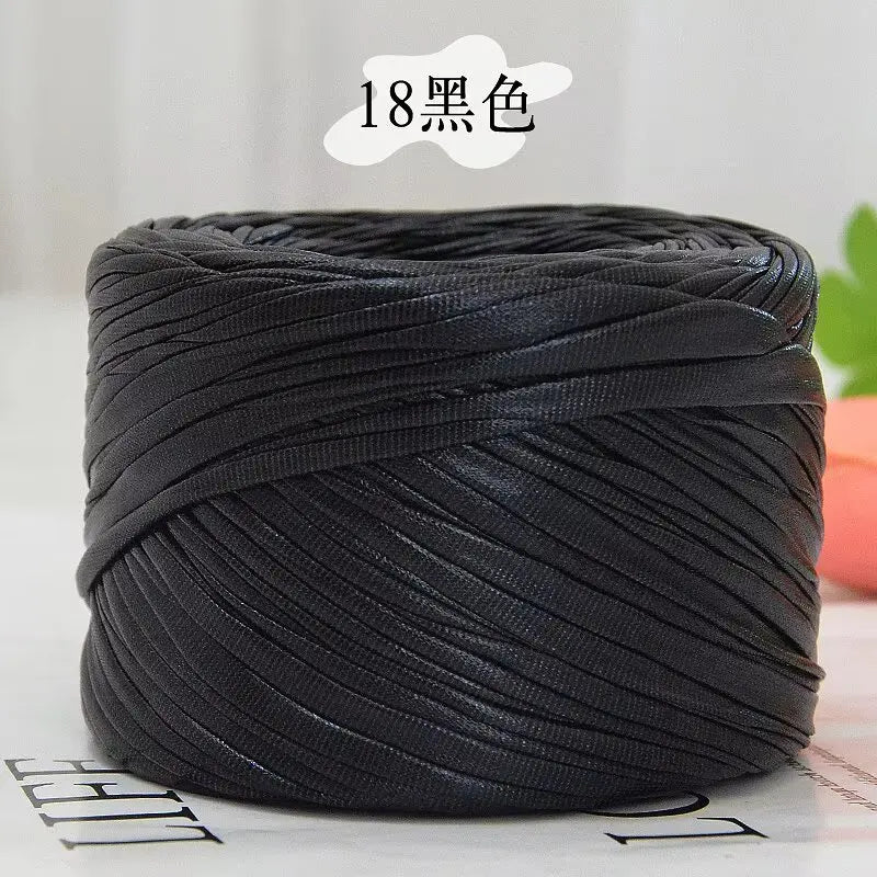 A ball of black metallic cake yarn for crafting is shown on a white surface.
