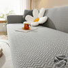 A thick gray jacquard sofa cover featuring white and orange decorative pillows on a light-colored sofa.