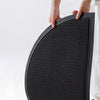 A hand is holding a black half-round non-slip PVC door mat with a textured surface.
