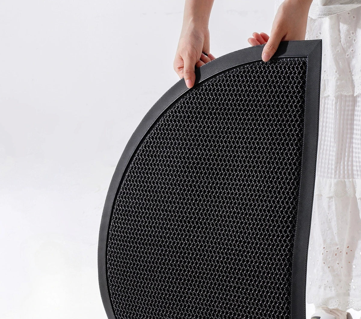 A hand is holding a black half-round non-slip PVC door mat with a textured surface.