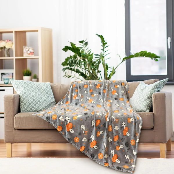 A gray coral fleece blanket with an orange and white animal pattern draped over a beige sofa.