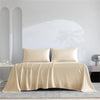 A beige luxury organic bamboo bed sheet set draped on a bed with white architectural details.