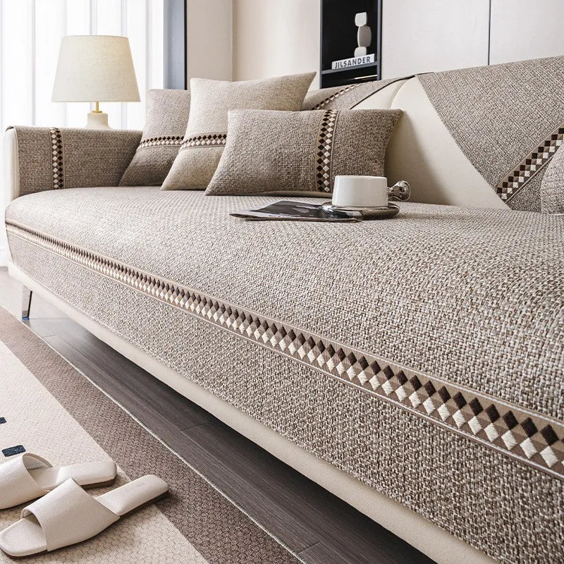 A beige linen sofa cover with decorative trim and pillows on a modern sofa in a living room.