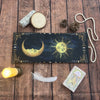 A dark blue tarot card storage pouch featuring a crescent moon and sun design, resting on a wooden surface.