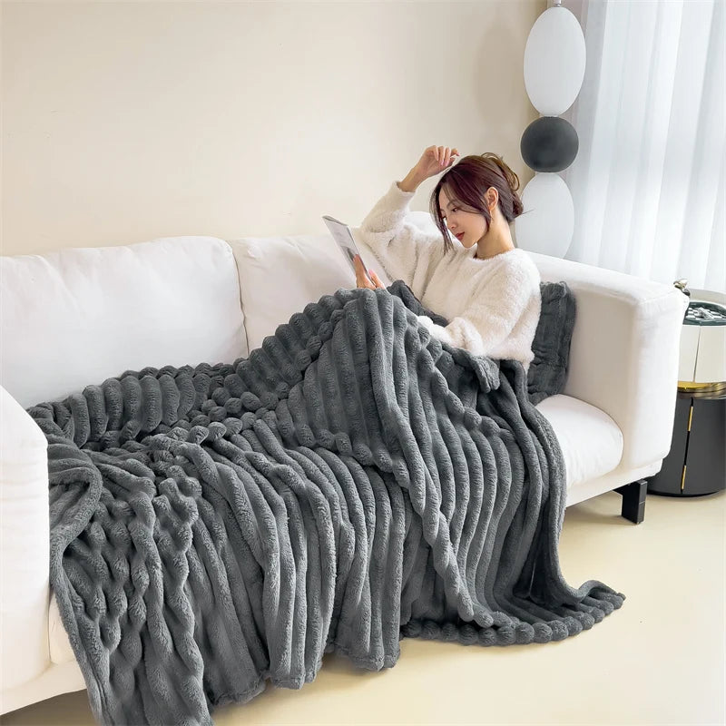 A woman is relaxing on a white sofa with a gray ultra-soft plush winter blanket draped over her.
