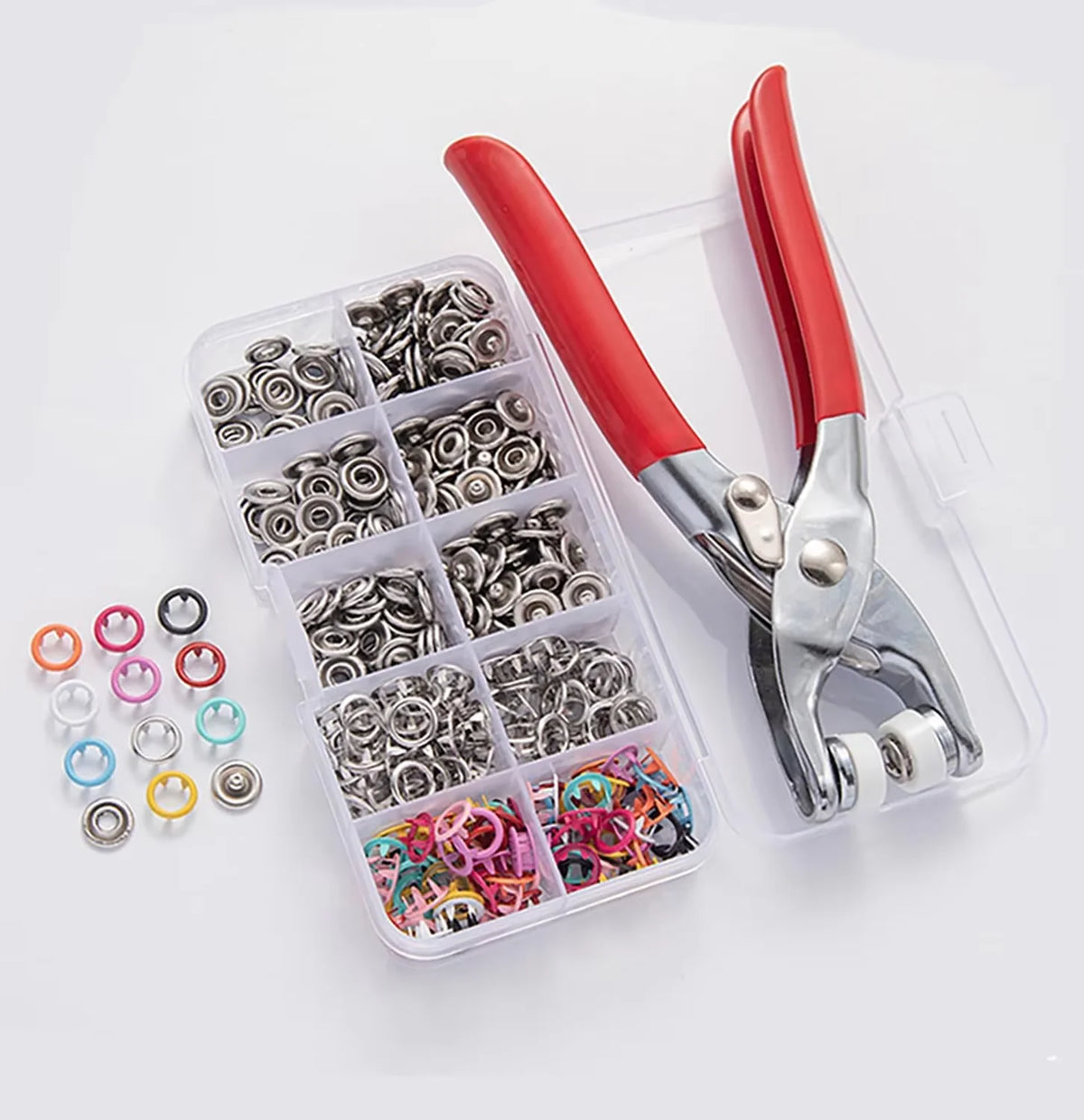 A pair of red-handled precision pliers holding various metal snap fasteners and rings in a clear plastic storage case.
