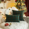 Two dark green tartan plaid decorative throw pillow covers resting on a white fluffy surface near a decorated Christmas tree.