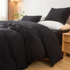 A black minimalist duvet cover is displayed on a bed with white bedding and wooden furniture.