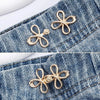 Gold-colored adjustable leaf clover waist tightener charms attached to denim fabric.