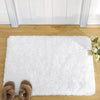 A fluffy white rug placed on a wooden floor with a white door frame in the background.