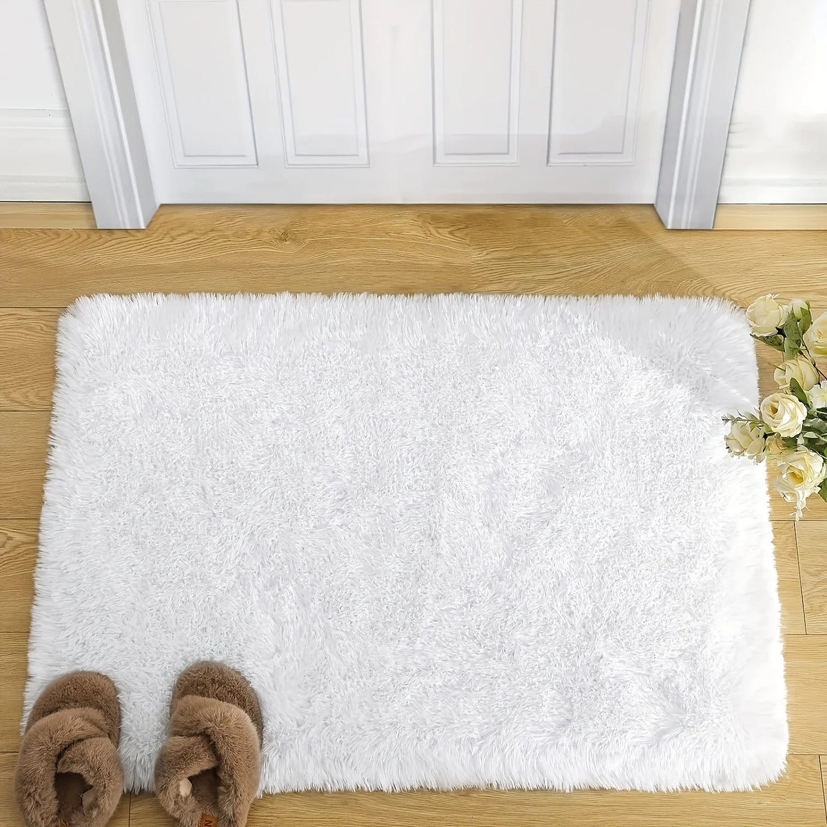 A fluffy white rug placed on a wooden floor with a white door frame in the background.