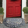 A vintage stone doormat with an intricate pattern lies on a gray stone step in front of a bright red door.
