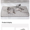 A fluffy gray kitten is lying on a gray cooling ice mat for pets.