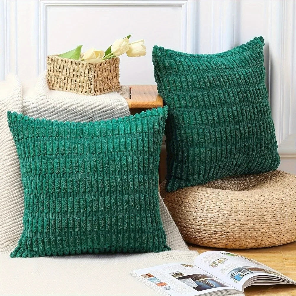 Two emerald green knitted throw pillow covers displayed on a light surface with natural woven accents.