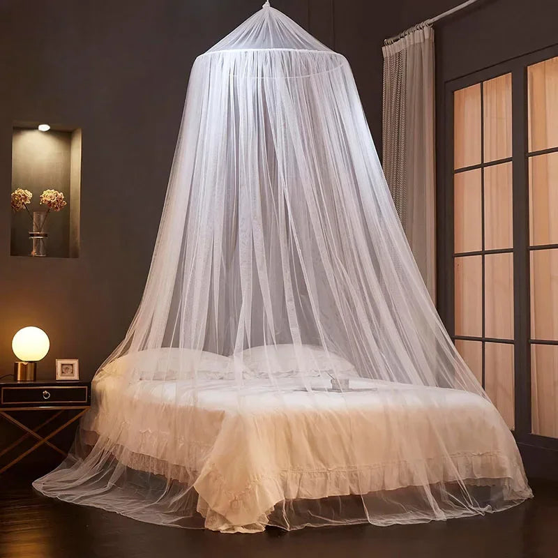 A sheer white floor-to-ceiling mosquito net canopy draped over a bed in a dimly lit room.