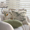 A collection of embroidered floral cushion covers in muted greens and creams displayed on a light-colored sofa.